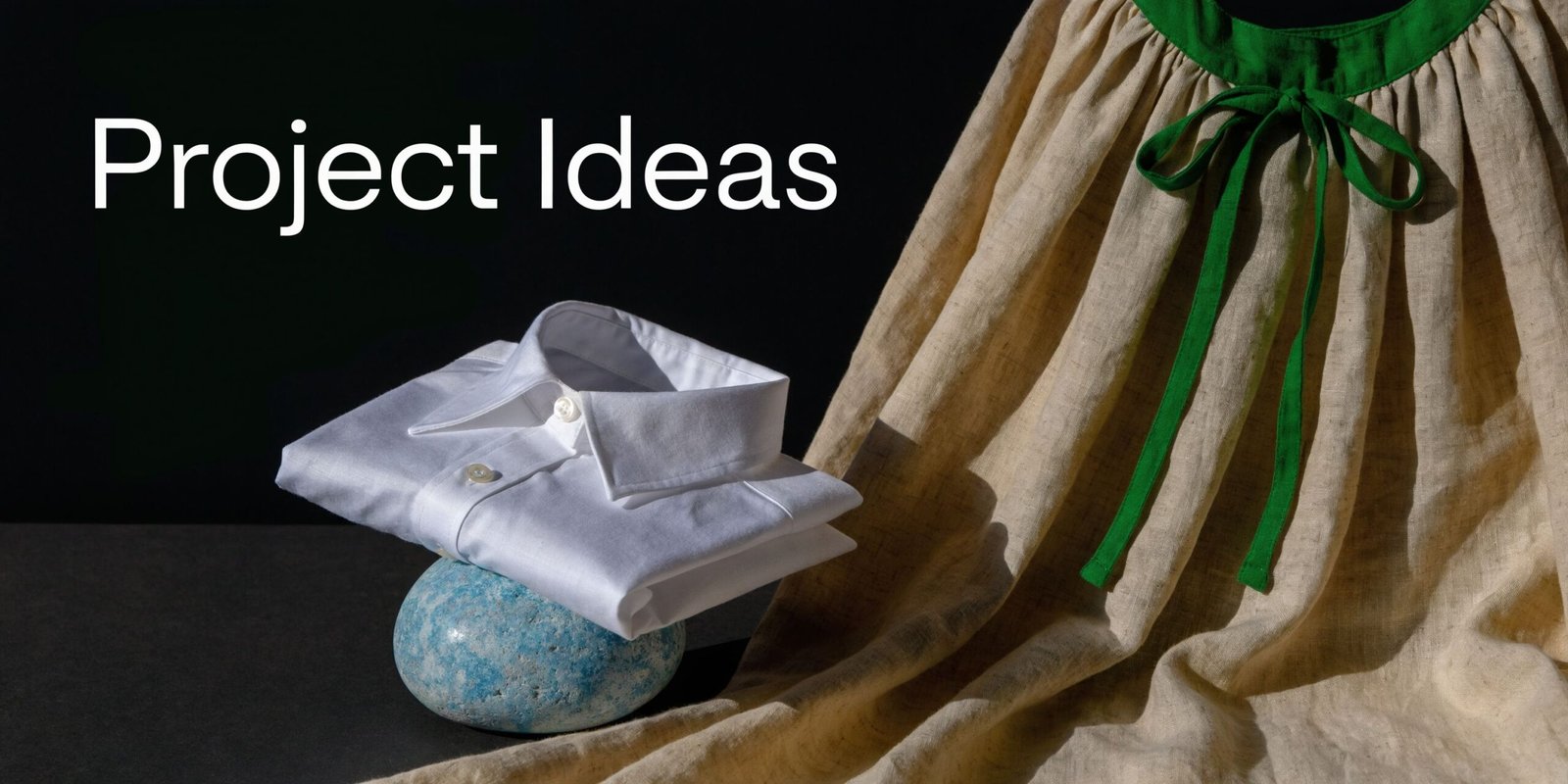 A folded white linen shirt resting on a blue decorative stone next to a draped beige fabric