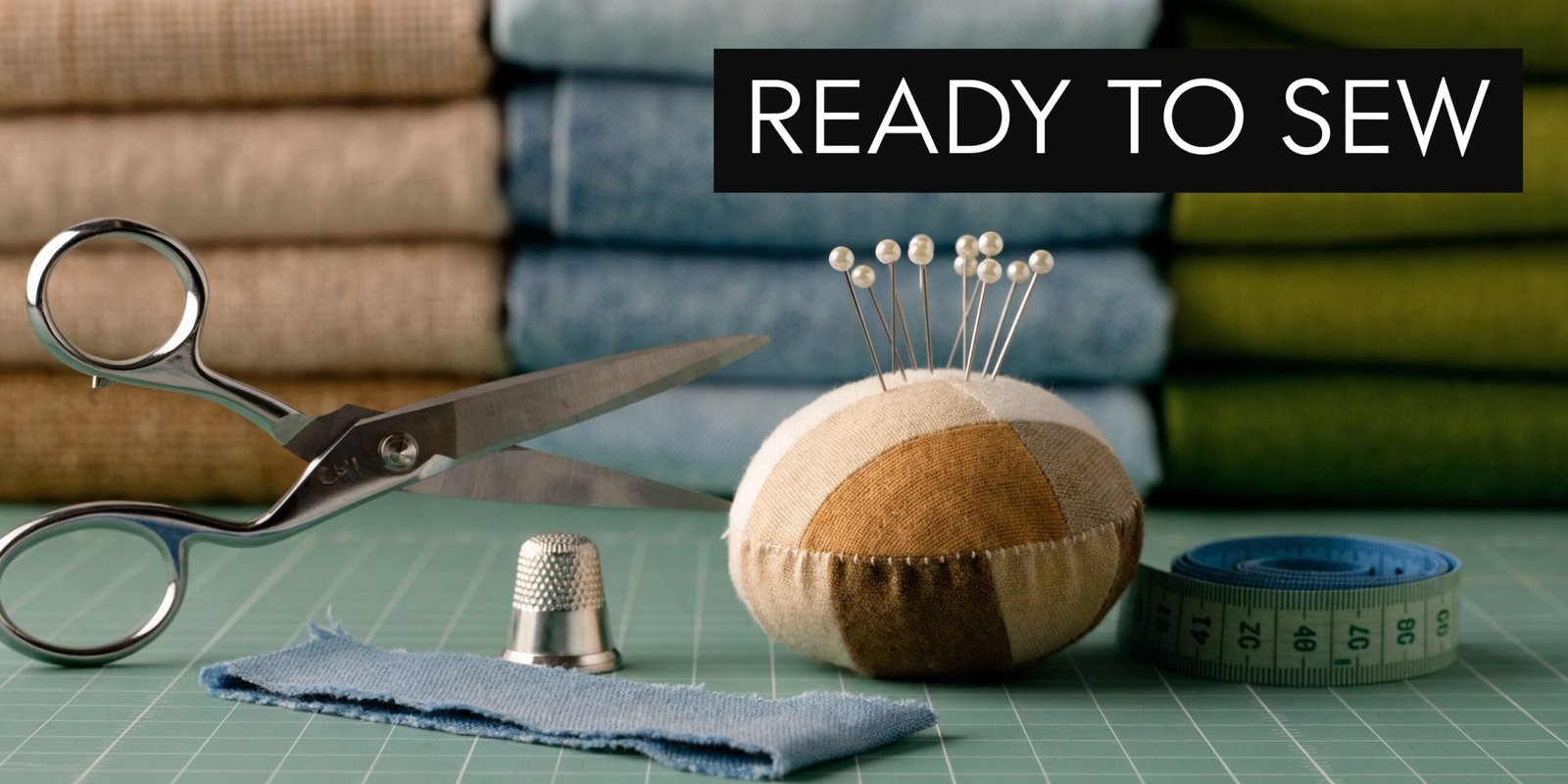 A close-up view of sewing tools including scissors, a pincushion, thimble, and measuring tape on a cutting mat.