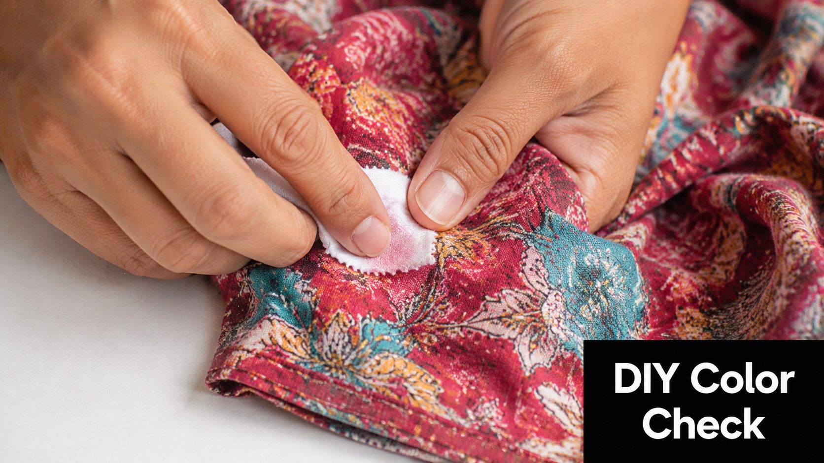 A pair of hands performing a color fastness test on a patterned fabric with a white cloth.
