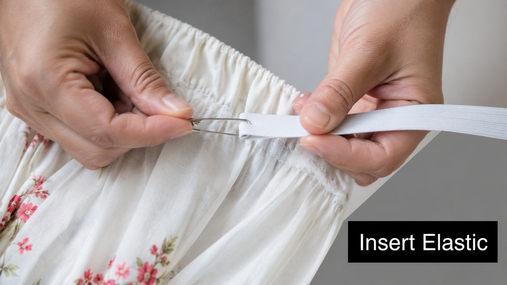 A person using a safety pin to guide white elastic through the waistband casing of a skirt.