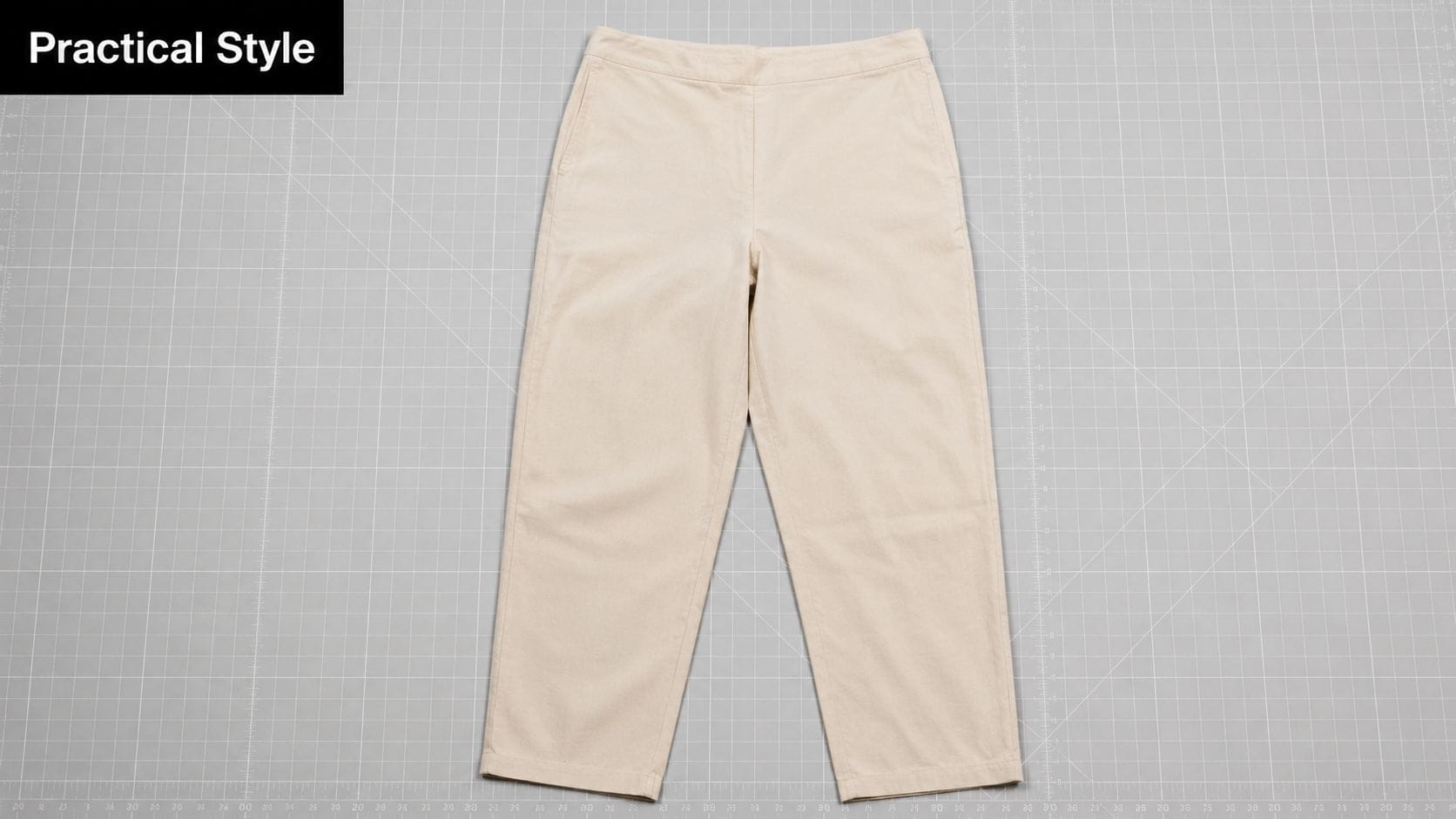A pair of light beige trousers laid flat on a grey grid cutting mat for pattern design.
