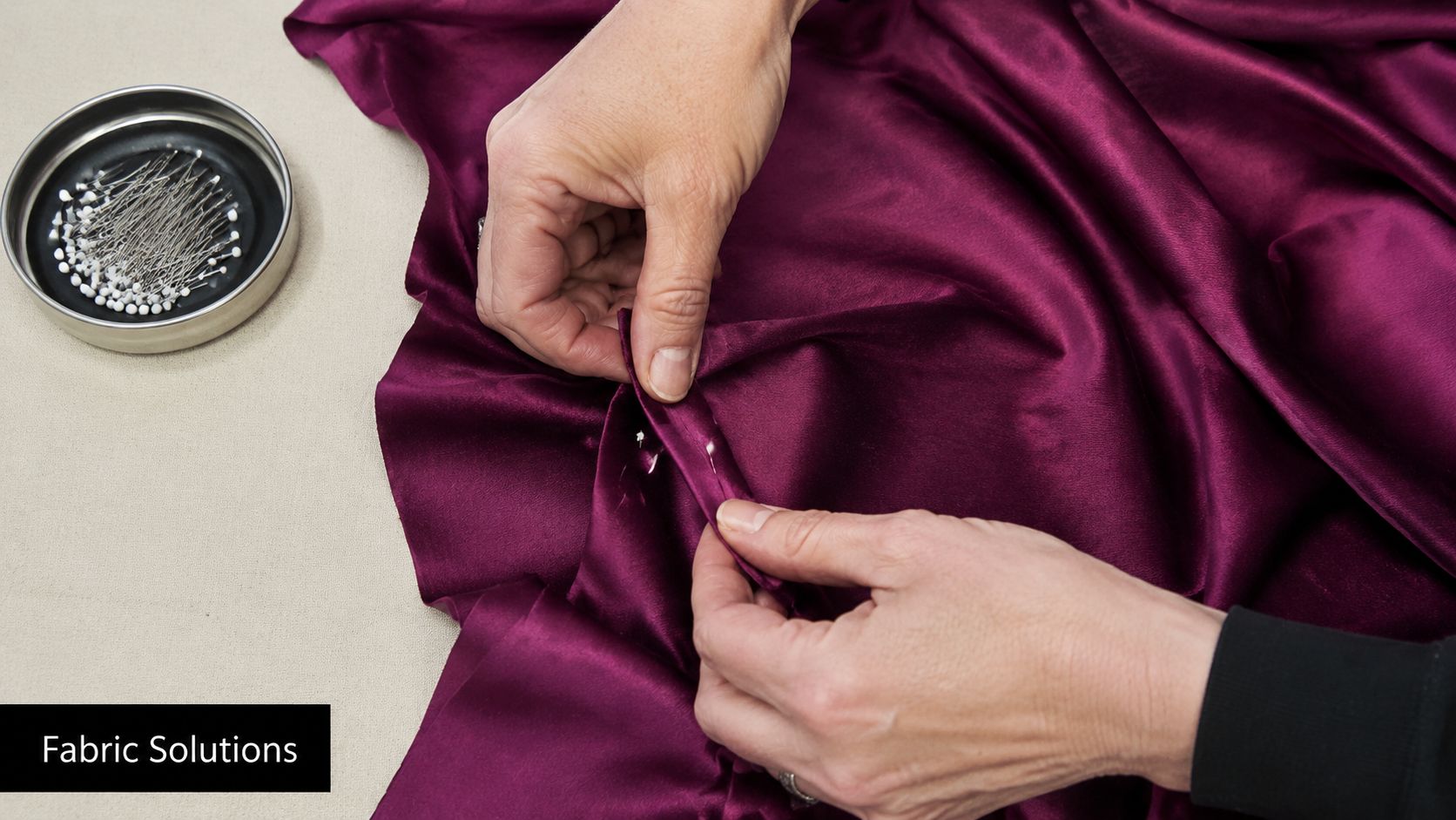 A close-up of a person's hands pinning a deep purple fabric to create precise pleats.