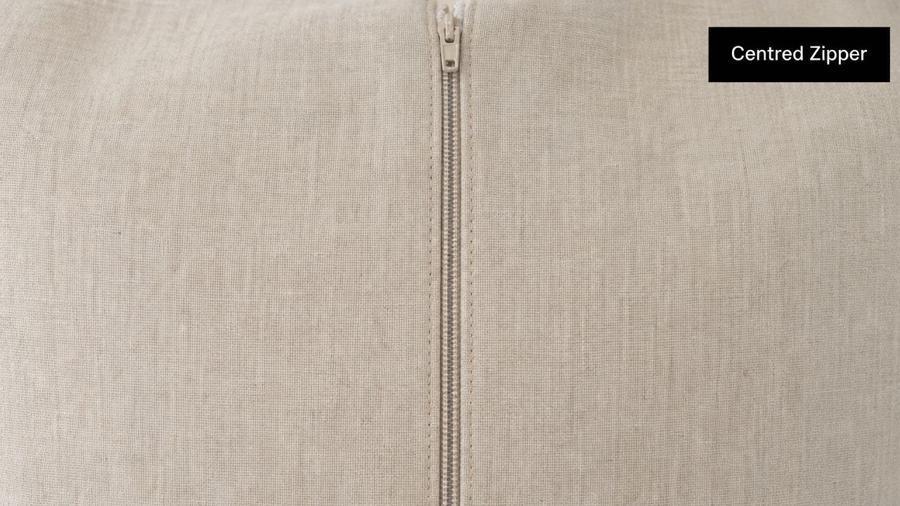 A close up view of a beige linen fabric pillow with a neatly sewn centred zipper closure.