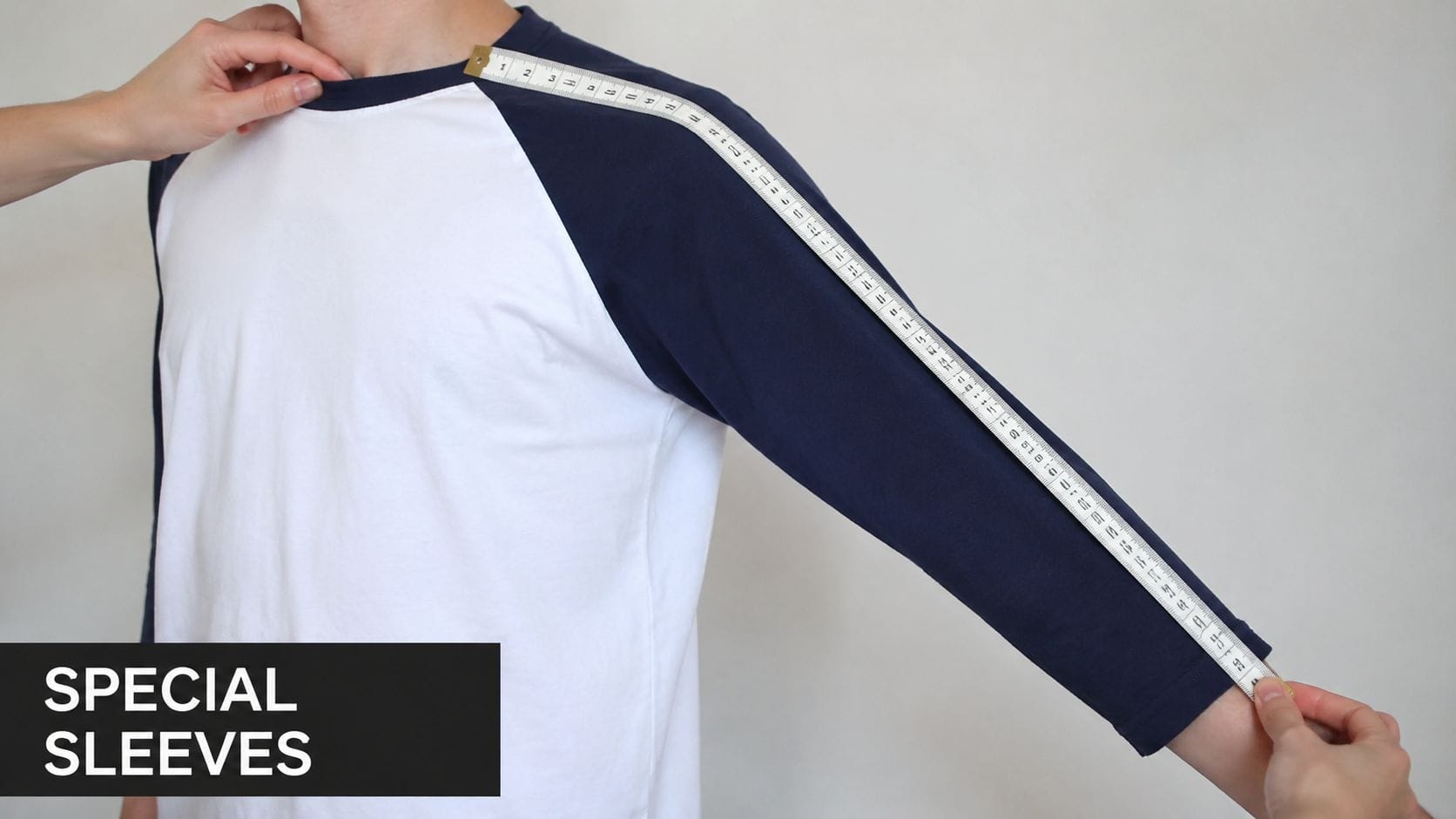 A measuring tape showing how to measure the raglan sleeve length on a two-toned shirt.