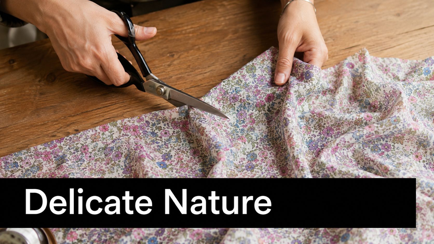 A close up view of hands using silver scissors to cut floral patterned fine cotton fabric.