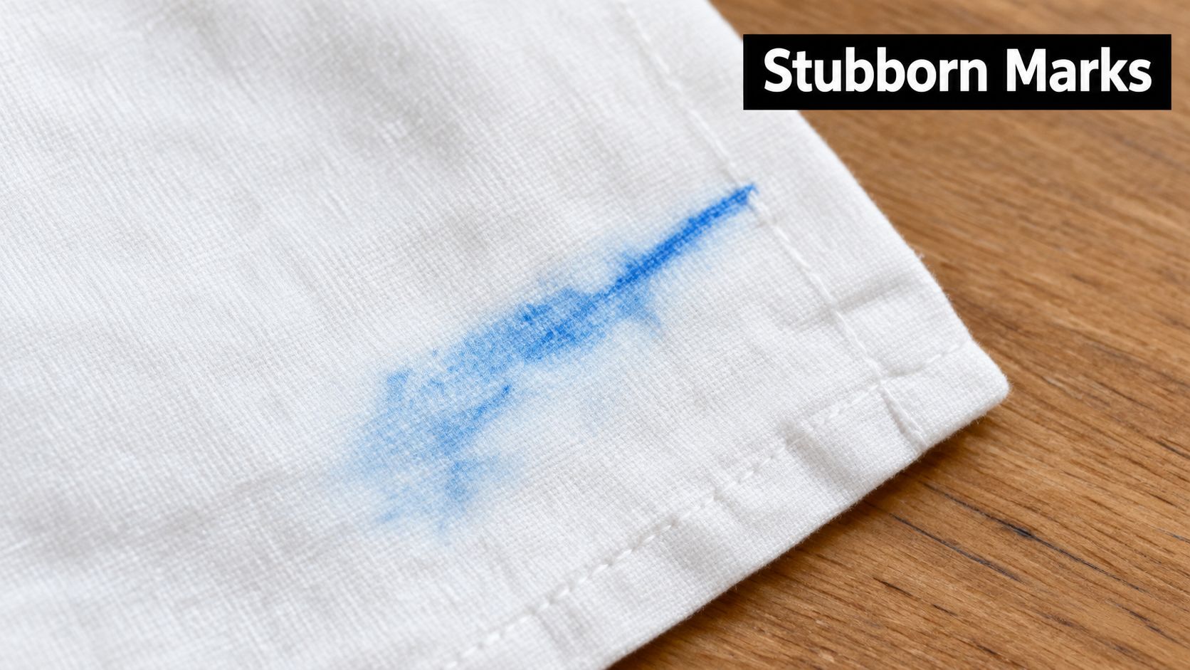 A close-up of blue ink stain on a piece of white fabric sitting on a wooden surface.